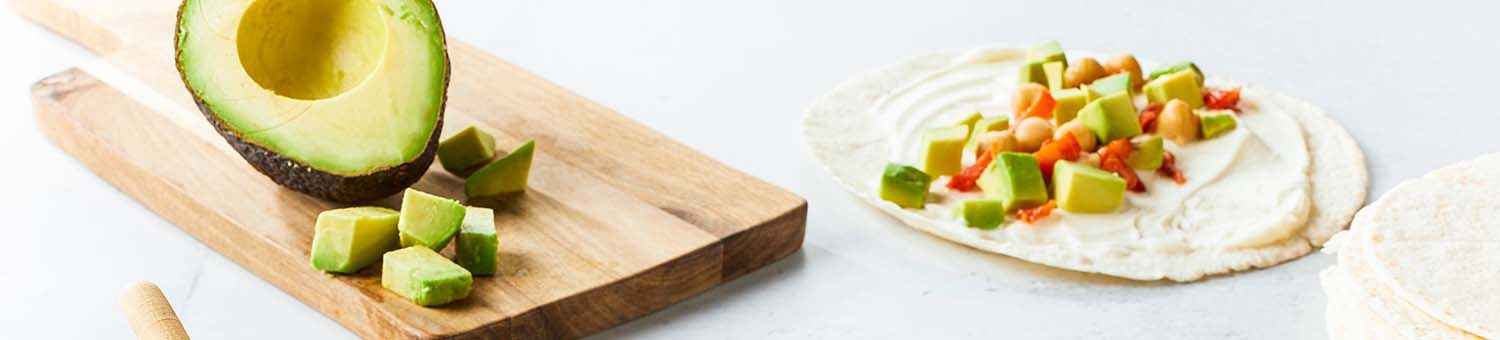 Wrap met zuivelspread, paprika en kip een opengesneden avocado op een houten snijplank